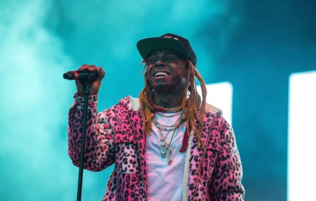 Lil Wayne wearing a pink leopard jacket performing on stage with a microphone in hand