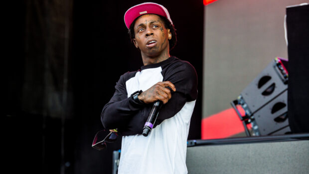 Lil Wayne wearing a red cap and holding a microphone on stage in a live performance