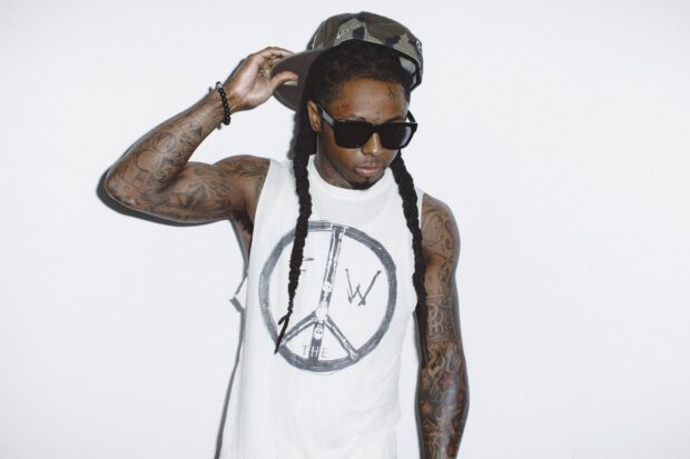 Lil Wayne with long braids wearing sunglasses and a sleeveless shirt with tattoos on his arms