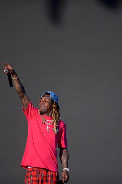 Lil Wayne wearing a red shirt and blue cap performing on stage with a microphone