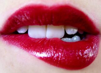 Close up of lips with bright red lipstick showing teeth and skin texture