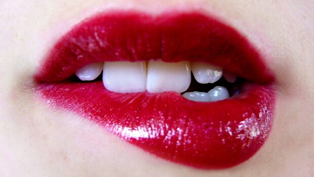 Close up of lips with bright red lipstick showing teeth and skin texture