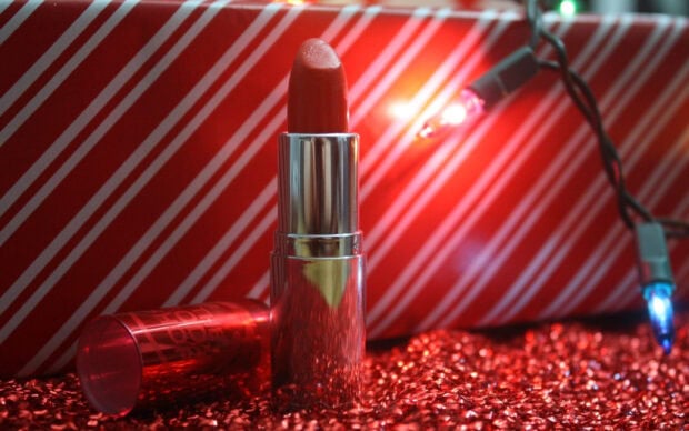 Red lipstick standing on glittering surface with festive lights and striped background