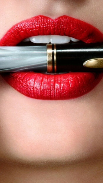 Close up of red lipstick on lips holding a lipstick tube between teeth