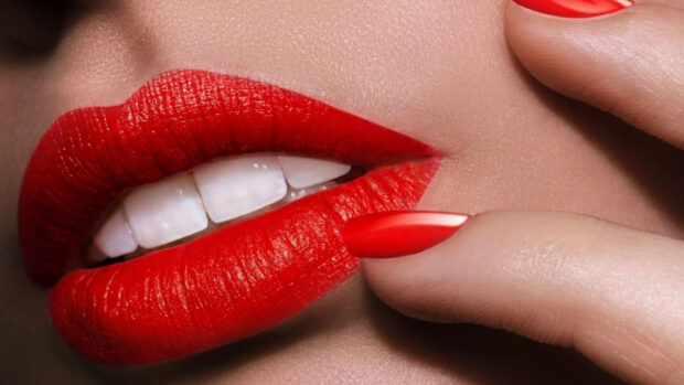 Close up of red lipstick on lips with matching nail polish and smooth skin