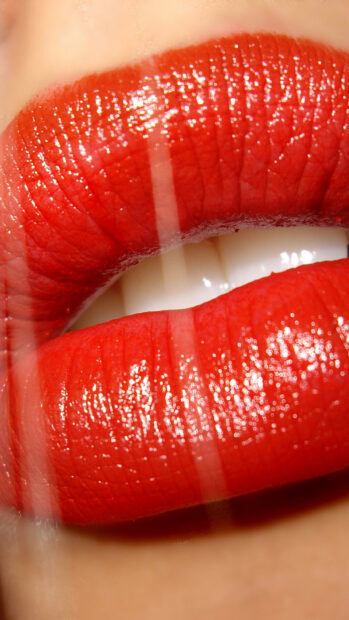 Close up of lips with shiny red lipstick and white teeth visible