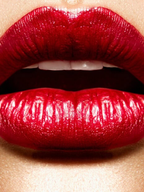 Close up of lips with shiny red lipstick applying makeup