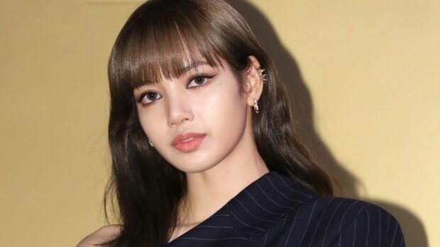 Lisa Blackpink wearing a pinstripe jacket and multiple earrings against a plain background