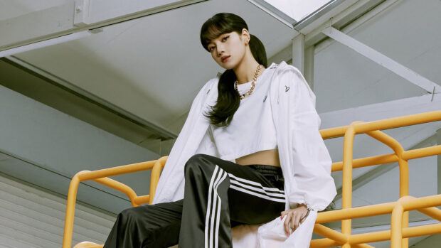 Lisa Blackpink wearing a white jacket and black pants sitting on yellow railing in an industrial setting