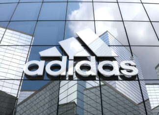White Adidas logo displayed on glass building reflecting cityscape and sky clouds