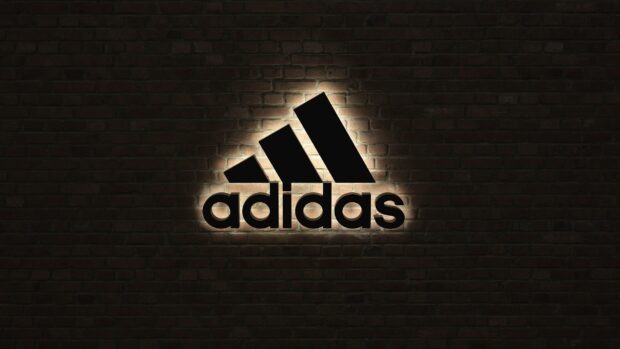 Black Adidas logo illuminated on brick wall background