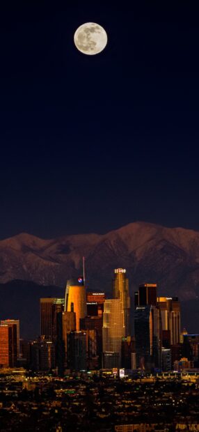 Full moon above Los Angeles skyline with snowy mountains in the background at night