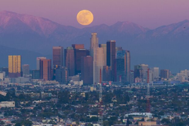 Full view of Los Angeles skyline with a large full moon and mountain range in the background