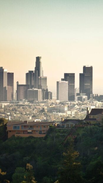 A scenic view of Los Angeles skyline with tall buildings and surrounding greenery at sunset