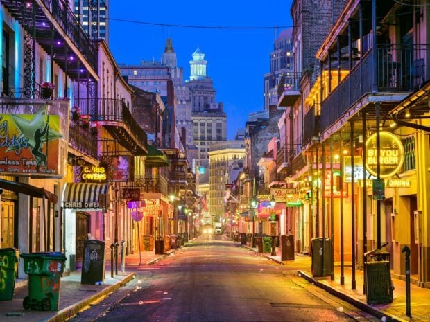 A vibrant street scene in Louisiana showing colorful buildings and neon signs at dusk