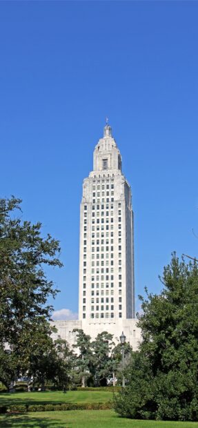 The Louisiana state capitol building standing tall with green trees and clear blue sky in the background