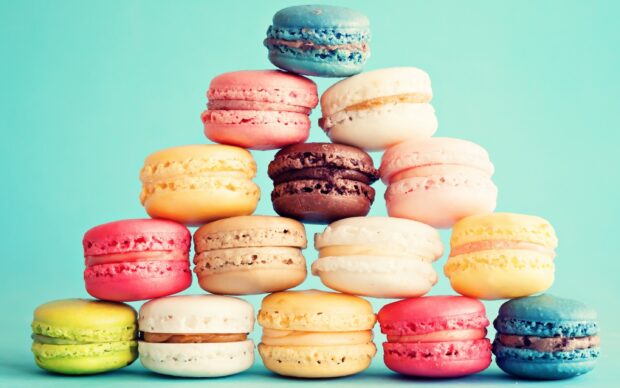 A colorful stack of assorted macaron desserts arranged in a pyramid shape against a blue background
