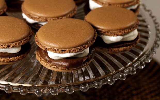 Close up of chocolate macaron with cream filling on glass plate