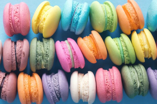Close up of colorful macaron assortment on a blue surface arranged in rows