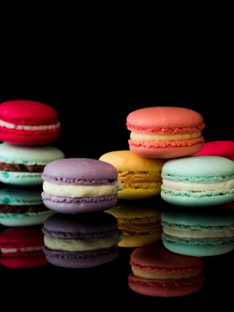 Colorful macaron assortment with creamy filling on reflective black surface showing macaron variety