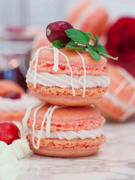 Two pink macaron desserts with cream and cherry decoration stacked on marble surface
