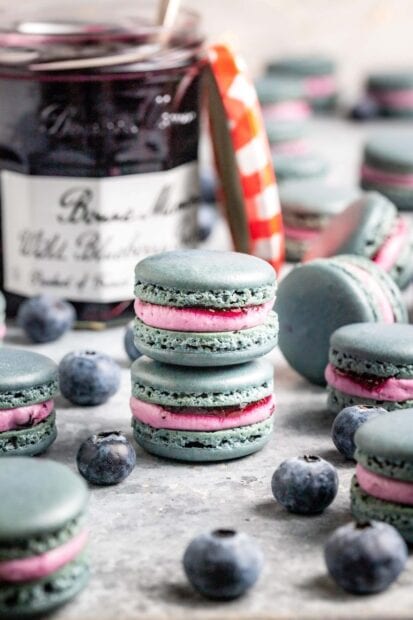 Blue macarons with pink filling surrounded by fresh blueberries and a jar in the background