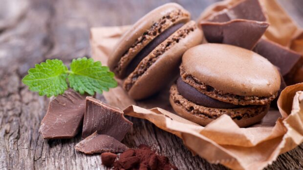 Chocolate macarons with fresh mint leaves and broken chocolate pieces on rustic wooden surface