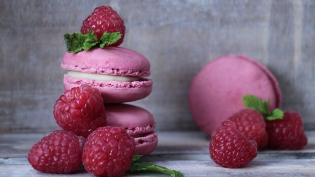 Pink macaron with fresh raspberries and mint leaves on a wooden surface