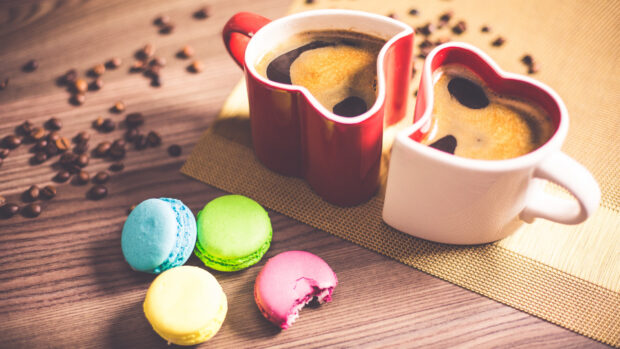 Colorful macaron with coffee beans and heart shaped cups on wooden table