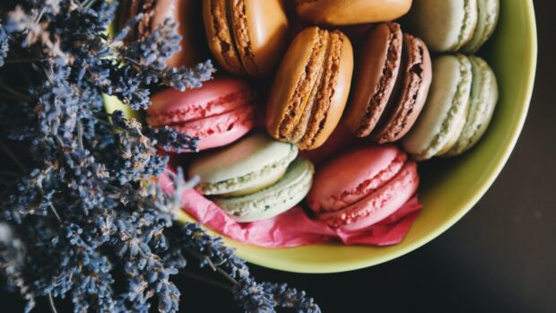 A close up of colorful macaron arranged in a bowl with dried flowers nearby