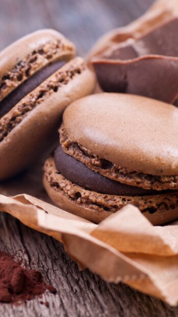 Close up of chocolate macaron with chocolate filling on rustic wooden table