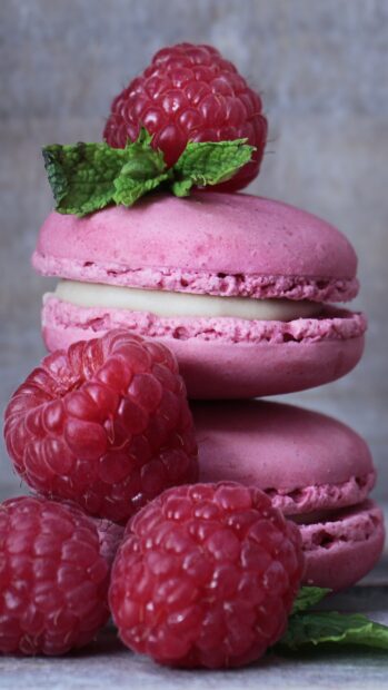 Pink macaron with raspberries and mint leaves stacked on a wooden surface