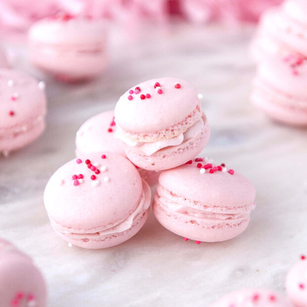 Pink macaron close up with creamy filling and colorful sprinkles on marble surface