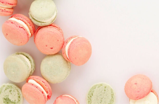 Pink and green macarons arranged on a white surface with creamy filling