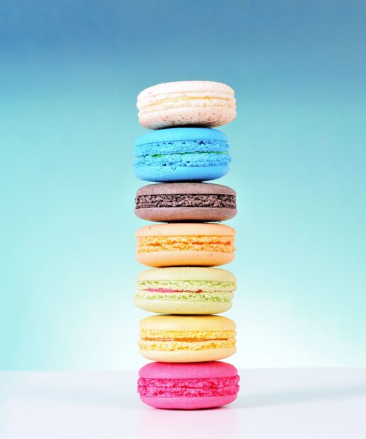 A stack of colorful macaron desserts with various flavors against a blue gradient background