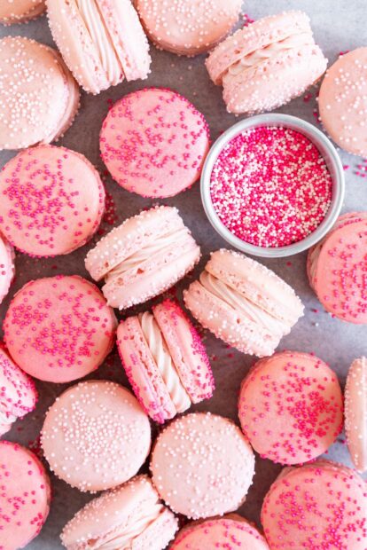 Pink macaron with white and pink sprinkles arranged with a bowl of colorful candy sprinkles