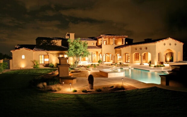 Luxury mansion at night with illuminated courtyard and swimming pool