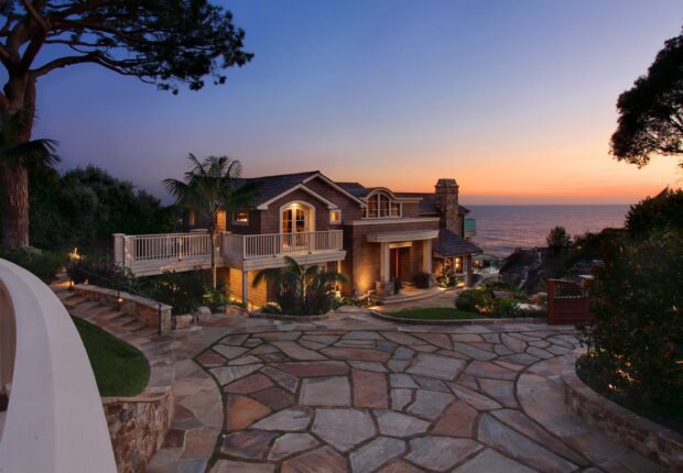 Elegant mansion surrounded by trees near the ocean at sunset with stone driveway and palm trees
