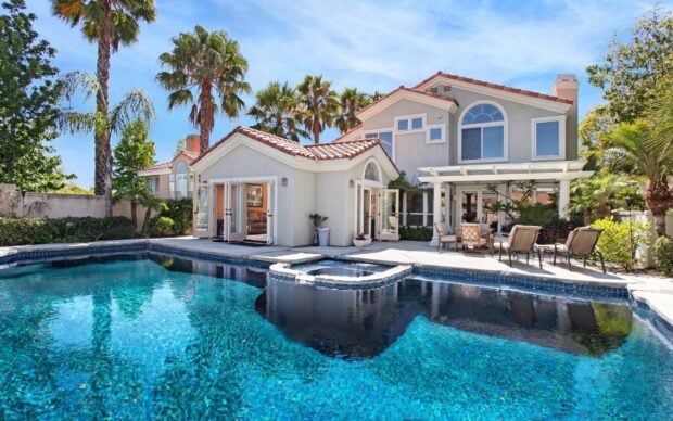 Luxurious mansion with a clear blue swimming pool and palm trees on a sunny day