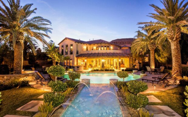 Luxury mansion with palm trees and illuminated garden at sunset