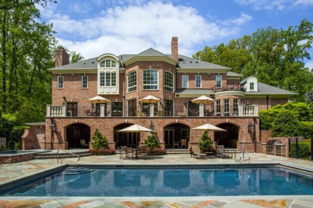 Spacious mansion with brick exterior and outdoor pool in a lush green setting