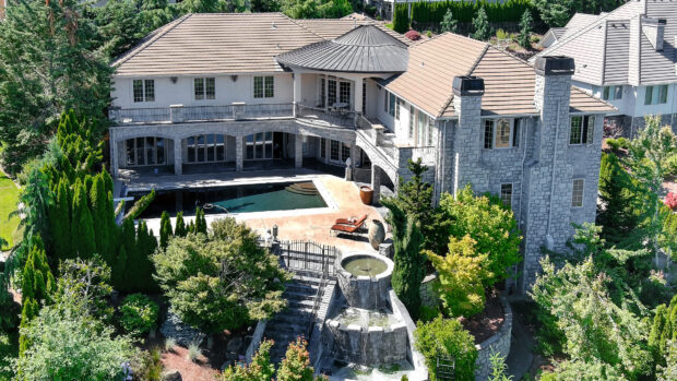 A large mansion surrounded by lush greenery and a stone water fountain in the garden