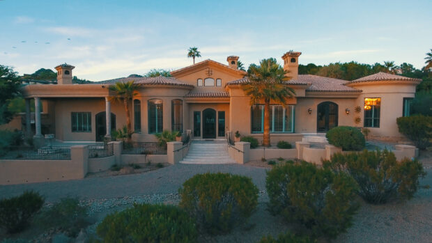 A luxury mansion surrounded by palm trees and desert shrubs under a clear sky