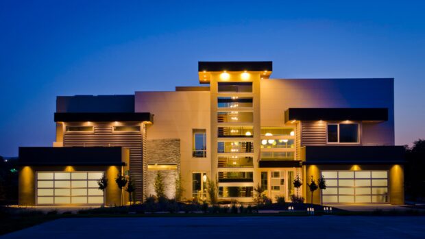 Modern mansion architecture with illuminated glass windows and garage doors at dusk