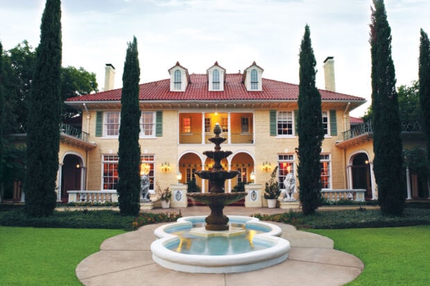 A grand mansion surrounded by tall trees and a decorative fountain in front