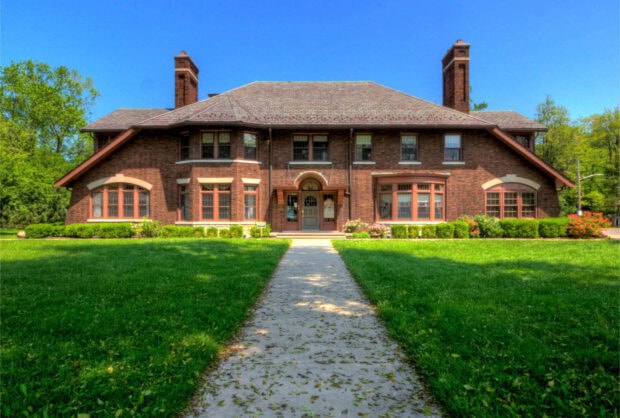 A mansion surrounded by green lawn and trees under a clear blue sky