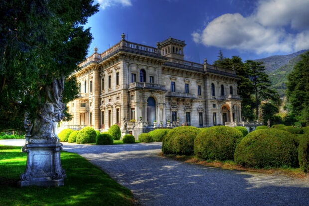 A mansion surrounded by trimmed bushes and trees under a blue sky