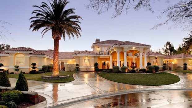Beautiful mansion with a palm tree and a wet driveway in a luxurious neighborhood
