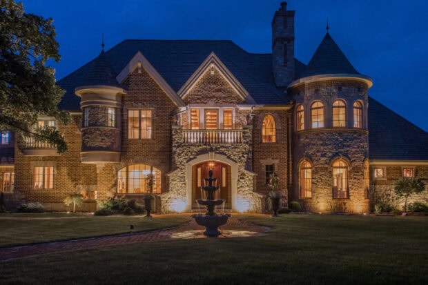 Elegant mansion with stone facade illuminated at night surrounded by a well maintained garden