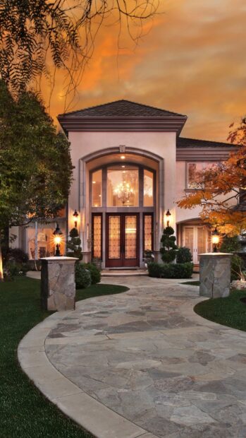 Large mansion entrance with stone path and illuminated lanterns at sunset